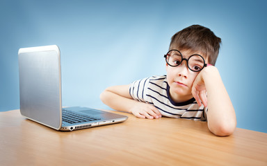 seven years old child in glasses sitting with a laptop at table