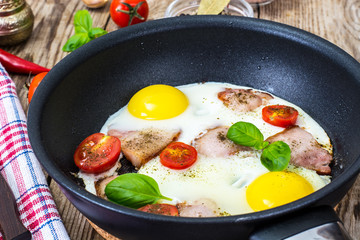 Fried eggs with bacon and tomatoes in a pan