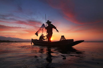 Silhouette of fishermen using nets to catch fish at the Bangpra lake with beautiful scenery of nature during sunrise time. Bang Pra Reservoir at Chonburi province in Thailand