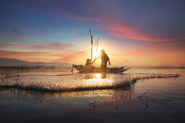 Obraz premium Silhouette of fishermen using nets to catch fish at the Bangpra lake with beautiful scenery of nature during sunrise time. Bang Pra Reservoir at Chonburi province in Thailand