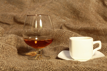 White cup of coffee and cognac or brandy in a glasses on Old textile sacking