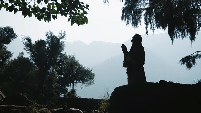 Silhouette of a praying man in a hoodie on nature background