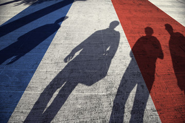 Shadows of group of people walking through the city streets with painted France flag on the floor.
