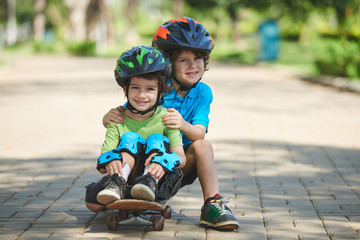 Lovely portrait of little brothers sitting together on skateboard and looking at camera with toothy smiles, blurred background