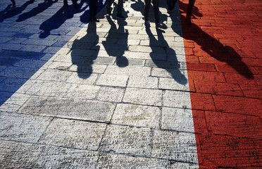 Shadows of group of people walking through the sunny street with painted France flag on the floor.