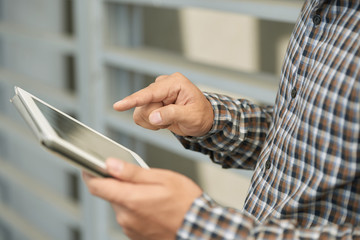 Close-up shot of young male hands working with documents on digital tablet, blurred background