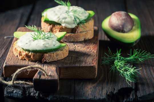 Tasty sandwich with avocado and tzatziki sauce on wooden board