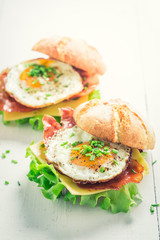 Tasty burger with bacon, eggs and cheese on white table