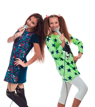 Two young girls girlfriends with long hair singing into two microphones on a white background