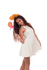 Lovely girl brunette with long hair in a white dress with a bow on her head with a big candy on a...