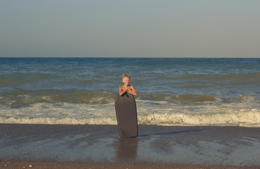 Funny caucasian boy with a board on the sea coast