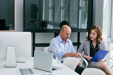 Obraz premium Middle-aged manager and his pretty young colleague sitting in office and working on business presentation