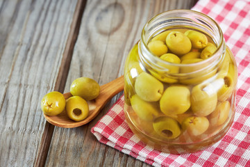 Pickled green olives in wooden spoon next to a jar of preserved olives. Copy space
