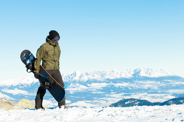 Fototapeta na wymiar Snowboarder walking at the top of a mountain with his snowboard in hand