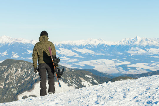 Snowboarder looking at a beautiful scenery from the top of a mountain