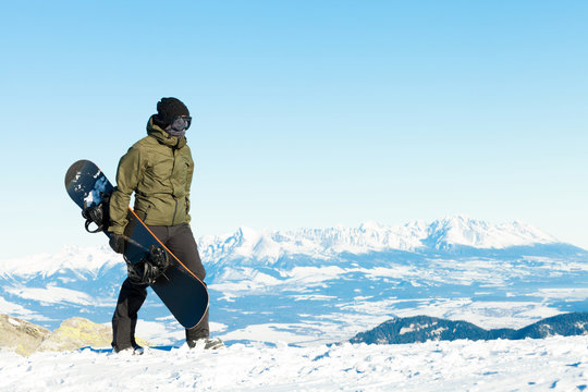Snowboarder walking at the top of a mountain with his snowboard in hand