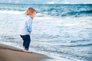 Cute baby boy  on the beach, admiring the sea. Bare feet.  Happy