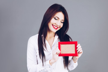 Beautiful brunette girl holding red photo frame in hands.