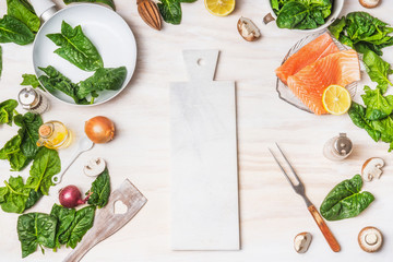 Healthy or diet  food background with cutting board, organic spinach leaves, salmon, pan ,fork and cooking ingredients on white kitchen table background, top view, place for text