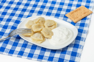 dumplings on a plate with sour cream and a fork on a blue tablecloth