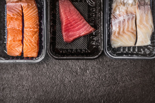 Selection of raw colorful fish fillets : salmon, tuna and codfish in plastic boxes on dark rustic background, top view, border, place for text. Healthy Seafood concept