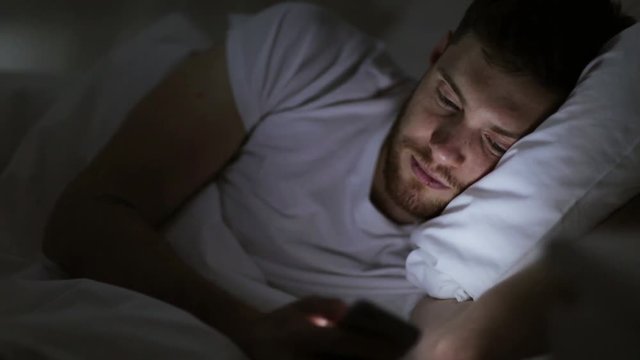 young man with smartphone in bed at night