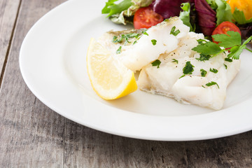 Fried cod fillet and salad in plate on wooden background
