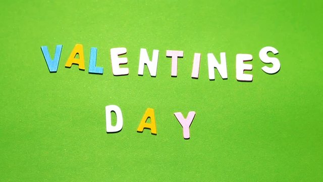 Wood characters of different colors arranged in a word Valentine's day on a green background with blur effect
