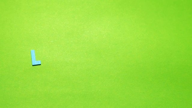 Wood characters of different colors arranged in a word love on a green background with hand slide
