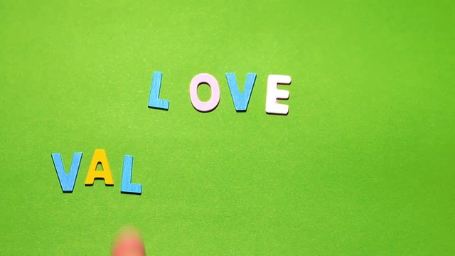 Wood characters of different colors arranged in a word love valentine's on a green background with hand slide
