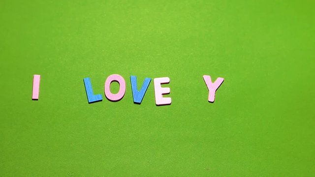 Wood characters of different colors arranged in a word I love you on a green background with hand slide
