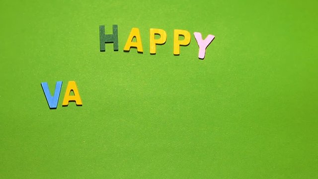 Wood characters of different colors arranged in a word happy valentine's day on a green background with hand slide
