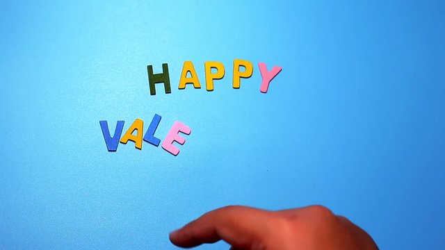 Wood characters of different colors arranged in a word happy valentine's day on a blue background with hand slide
