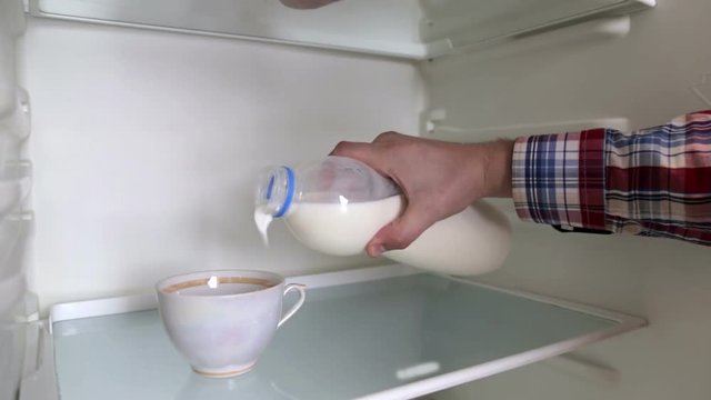 Man is pouring milk into a cup, in the refrigerator
