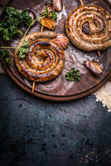 Grilled spiral sausages with garlic and seasoning on dark wooden background, top view, place for...