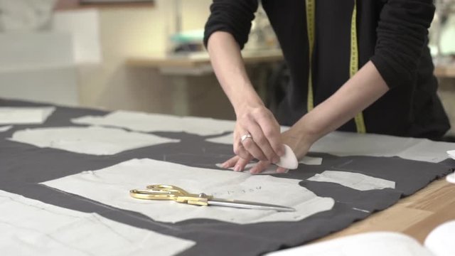 Female Caucasian hands in black dress passing round pieces of grey fabric with French chalk lying on table in sewing classroom in slowmotion