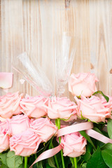 Pink blooming fresh valentines day roses with ribbon on wood with two champagne glasses