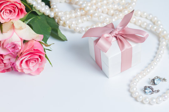 Gift box with pink ribbon with jewellery and roses on white table