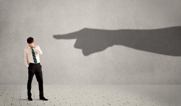 Business person looking at huge shadow hand pointing at him conc