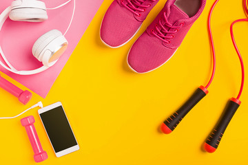 Fitness accessories on yellow background. Sneakers, dumbbells, headphones and smart.