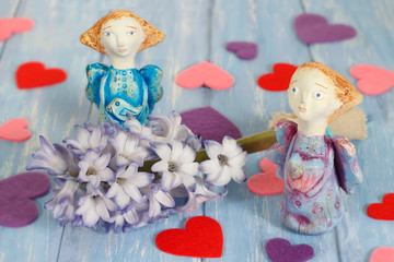 Fototapeta na wymiar Two ceramic clay angels near hyacinth flower and hearts on shabby blue wooden planks in rustic style.