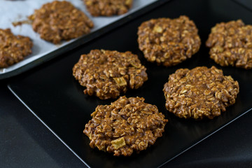 Golden oatmeal cookies with apple and nuts on a black plate and on baking paper.