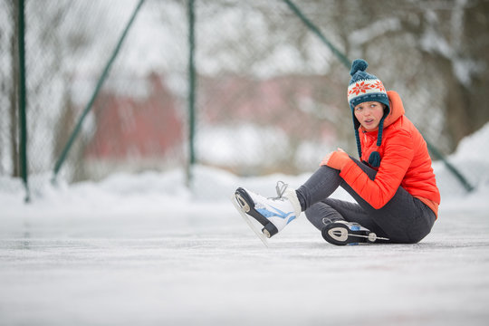 Ice skating concept - young woman sitting on the ice rink