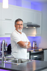 Fototapeta na wymiar Senior man standing in his renovated, modern kitchen,