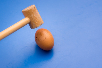 Egg about to be broken by a wooden hammer, blue background. 