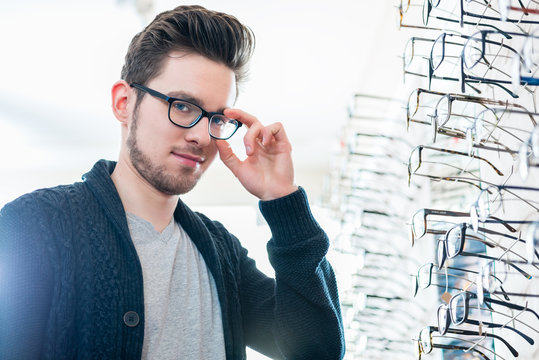 Mann vor Regal mit Brillen im Optiker Laden schaut in die Kamera