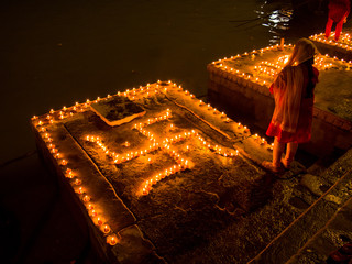 A woman stands next to  swastika decoration of clay lamps (diya) in Varanasi (India) on the festival of Dev Diwali - obrazy, fototapety, plakaty