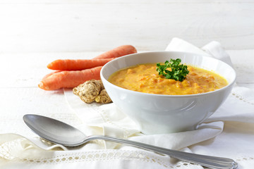 Carrot soup with ginger and parsley garnish, white wooden background