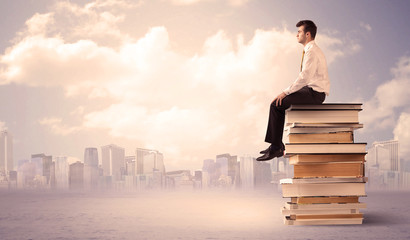 Man sitting on pile of books above city