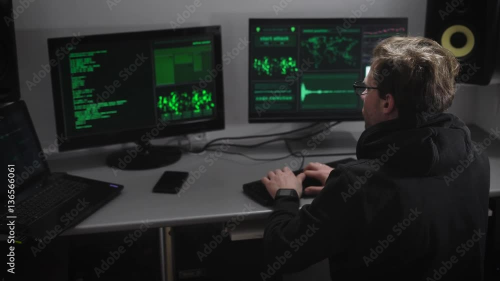 Poster villain hacker analyzes illegally obtained data on the monitor screens for creating spy software. yo